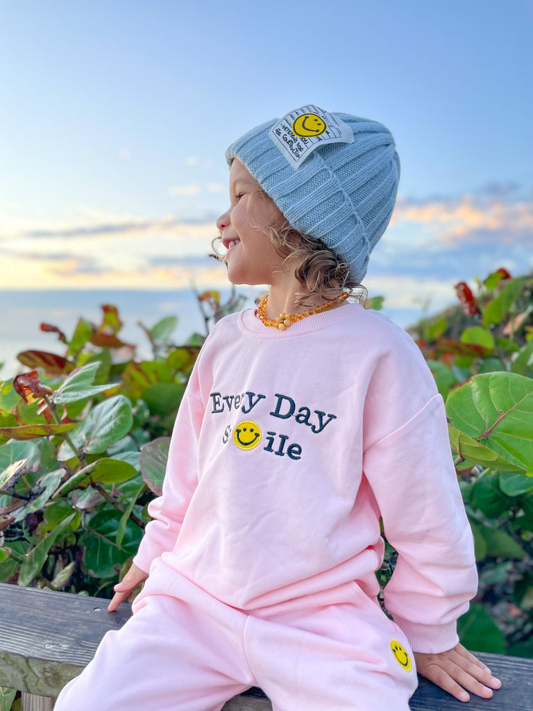 Baby girl wearing a smiley ribbed beanie in baby blue and a smiley sweatshirt matching set