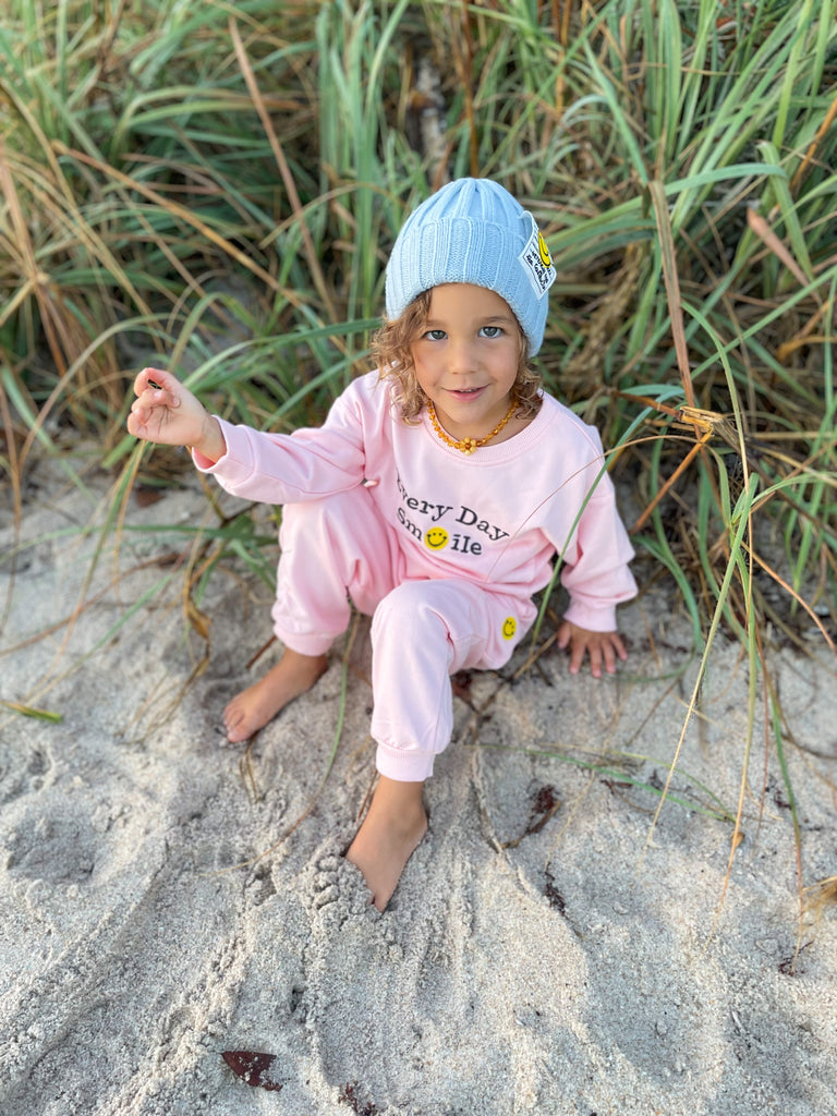 Baby girl wearing a Smiley face sweatshirt and joggers pants set in pink with a Smiley face ribbed beanie