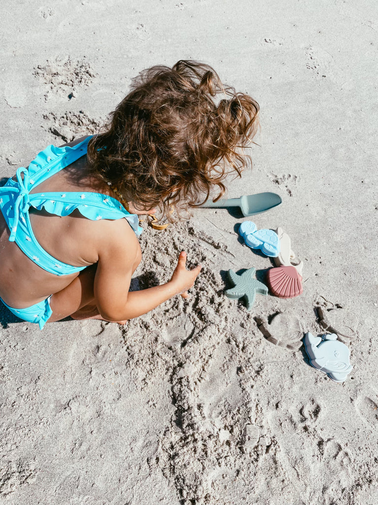Baby girl playing with silicone sand toys on the beach 